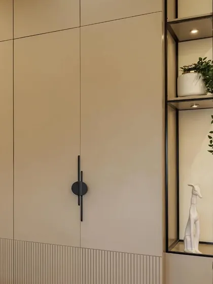 A detail of the beige wardrobe with modern black designer handles and fluted paneling. The attached metal open shelving adds an industrial touch and functional display space.