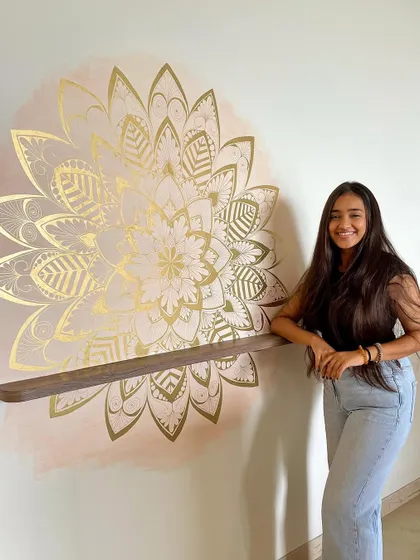 Posing with a finished golden mandala mural. The metallic gold leaf on a soft watercolor background creates a luxurious and radiant effect, perfect for a statement wall.