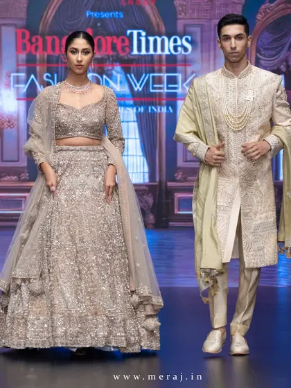 A full view of the coordinated runway look. The groom's gold raw silk sherwani and the bride's matching lehenga, both with intricate hand embroidery, create a statement of modern opulence and timeless elegance.