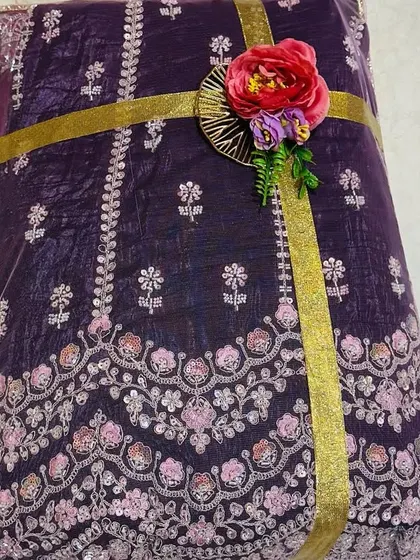 The details make all the difference. This close-up shows a richly embroidered purple fabric, perfect for a bridal lehenga, secured with a simple gold ribbon and a delicate floral accent to complement its intricate design.