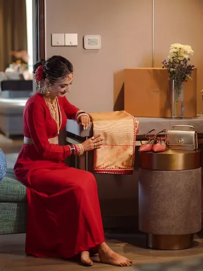 A bride in a stunning red saree, admiring her wedding attire and accessories before getting ready.