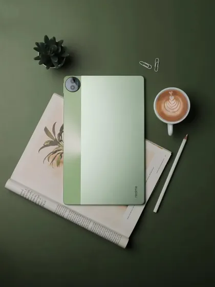 A top down flatlay of the realme Pad 2, a coffee, and a book, creating a complete lifestyle scene.