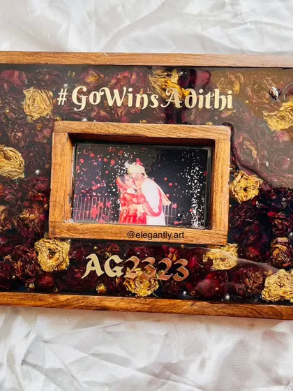 A close-up of a teakwood frame preserving a wedding garland with the couple's hashtag and initials. The details show the care taken to arrange each flower and element perfectly.