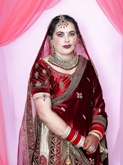 A classic bridal portrait against a simple pink backdrop, which makes the rich red of her velvet lehenga stand out.