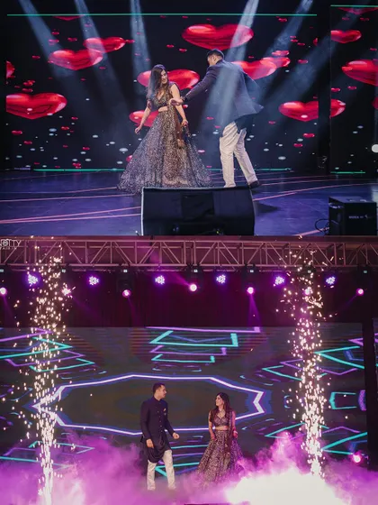 The couple performing on a multi-level stage with a heart-themed LED background. We capture the impressive production value of your Sangeet night.