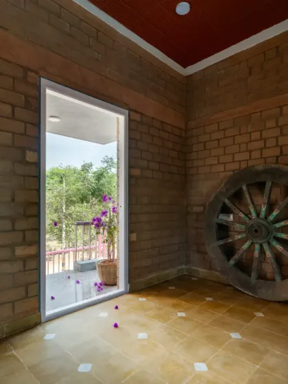 A doorway in the EESHA house frames a view of the green outdoors, contrasting with the earthy texture of the unburnt mud brick walls.