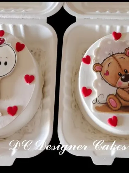 A pair of adorable bento cakes perfect for Valentine's Day or an anniversary. These mini cakes feature cute, hand-drawn style characters holding hearts, all packed in individual boxes.