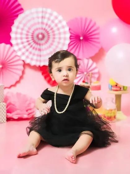 A stylish birthday girl in a black dress and pearls, looking elegant and chic during her first birthday photoshoot.