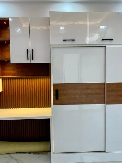 A complete bedroom unit featuring a sliding wardrobe integrated with a study table and display shelves. The white and wood combination is timeless.