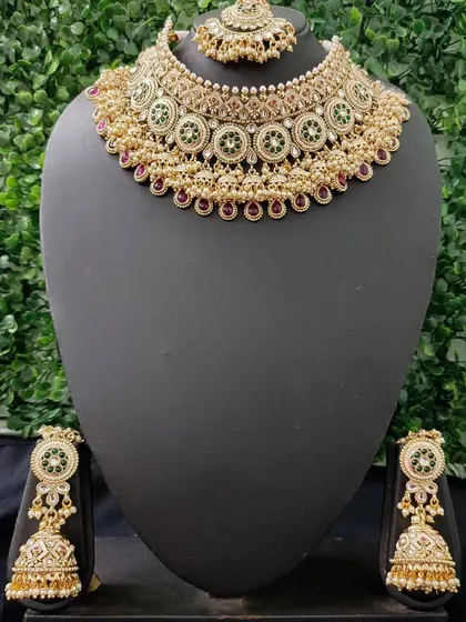 This elegant rental set features a beautiful choker with circular green and red motifs. The matching jhumkas complete the look, making it a versatile choice for any wedding function.