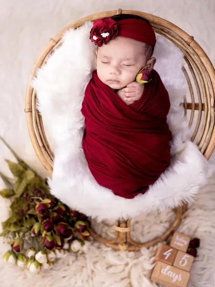 This newborn is wrapped snugly in a rich red swaddle, resting in a rustic cane basket. The color contrast and textures make for a visually striking portrait.