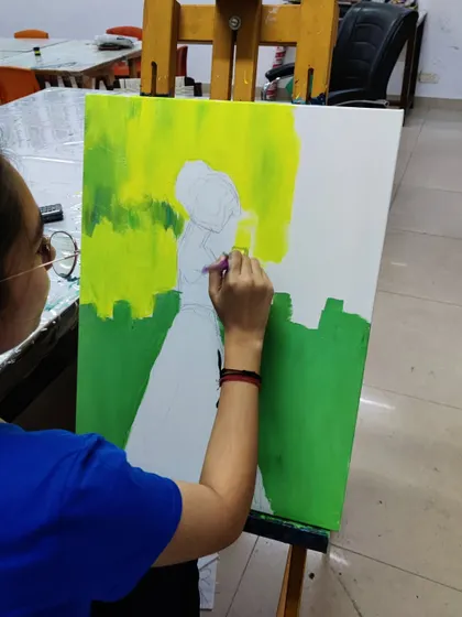A slightly different angle of the same painting in progress, showing the student carefully outlining the figure against the bright green background.