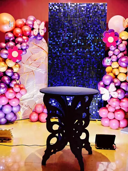 This butterfly-themed decor combines several elements for a high-impact look. It features large butterfly wing cutouts, colorful chrome balloon columns, and a sparkling blue sequin panel, creating a vibrant and dynamic photo corner.