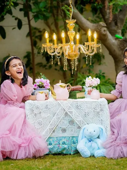 Laughter and joy at a whimsical outdoor tea party for two sisters. We believe in creating experiences, not just photoshoots, which allows for genuine moments like this to unfold naturally.