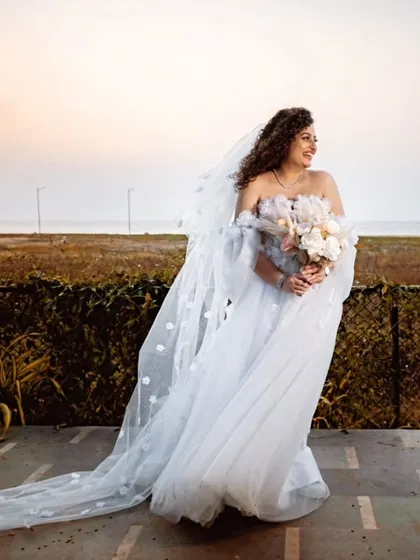 A windswept moment by the sea. The bride's ethereal gown and long veil flow beautifully in the breeze.