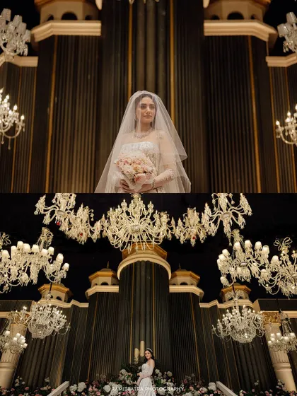 A bride stands in a grand hall in Bangladesh, dwarfed by magnificent chandeliers, creating a sense of awe and opulence.