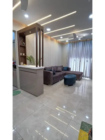 A wide shot of the living room, showing the false ceiling with profile lights, the custom partition, and the seating area.