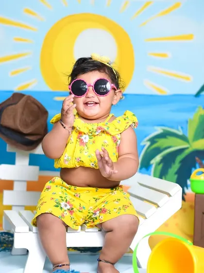 Aarna is all sunshine and smiles in our beach-themed studio shoot. The setup includes a beach chair, sunglasses, and a bright, sunny backdrop.