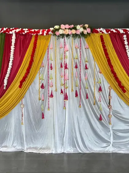 This is a vibrant backdrop perfect for a Haldi or Mehendi ceremony. I layered colorful drapes in green, yellow, and red, and added details like flower garlands and small Rajasthani umbrellas for a festive look.