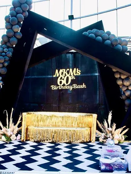 This 60th birthday bash had a chic black, gold, and white theme. The geometric stage, fringed gold sofa, and chevron-patterned floor created a sophisticated and modern look for the milestone celebration.