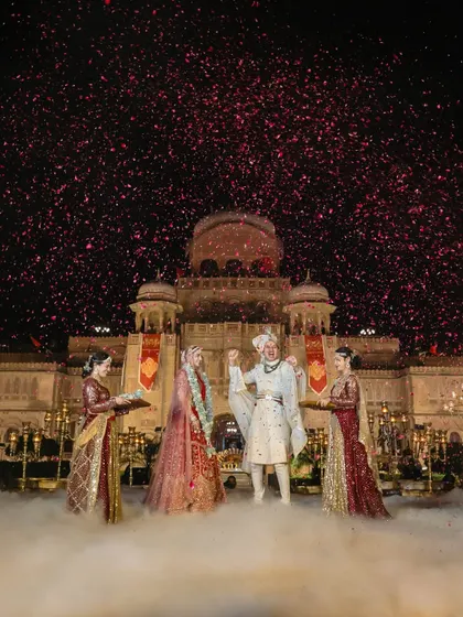 A moment of pure triumph and joy as the couple stands before the palace, surrounded by fog and a shower of pink confetti after their Varmala.