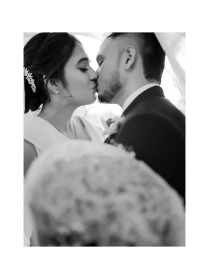 A classic black and white photo of the bride and groom sharing a kiss under the veil, a timeless and romantic wedding portrait.