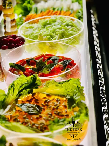 A fresh and vibrant salad bar setup. I offer a variety of crisp lettuces, toppings like cherry tomatoes and basil, and delicious dressings, providing a healthy and customizable option for guests.