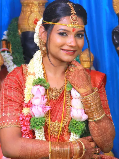 A traditional bridal pose, showcasing the bride's red saree, lotus garlands, and henna.