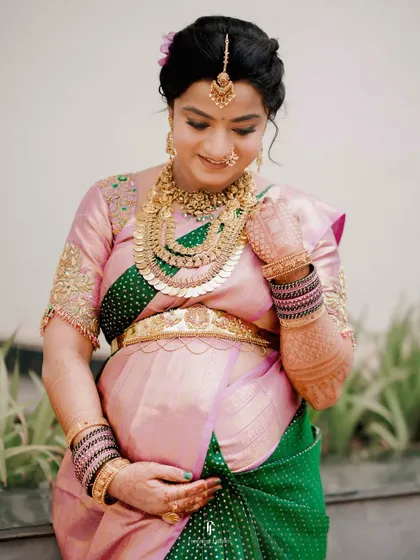 A classic portrait of a mother-to-be during her Seemantham ceremony. She gently holds her baby bump, adorned in a traditional silk saree and exquisite temple jewelry, embodying the grace of motherhood.