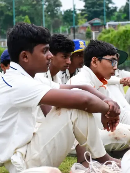 Young cricketers, with dirt on their whites, listen to their coach, a sign of a hard day's work on the field.