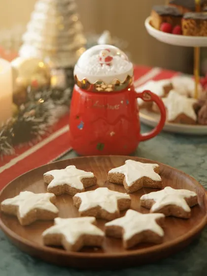 Star-shaped Christmas cookies on a wooden plate, next to a festive Santa mug, creating a cozy and whimsical holiday mood.