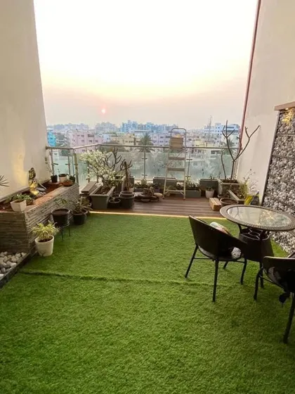 A full view of a transformed balcony, featuring a lush artificial grass floor, a stone-clad water feature, a gabion wall accent, and comfortable seating. This is a perfect example of a complete balcony makeover.