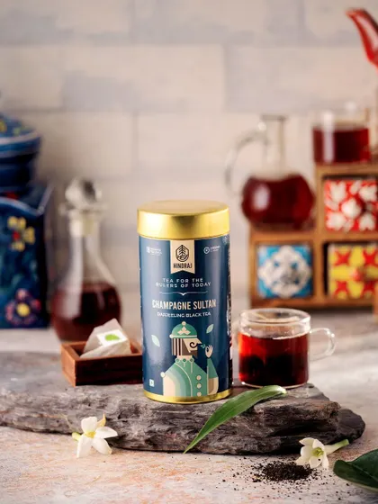 Hindraj's Champagne Sultan tea tin styled on a piece of slate with a colorful tiled background. This composition blends rustic and traditional elements to create a visually interesting and culturally rich product shot.