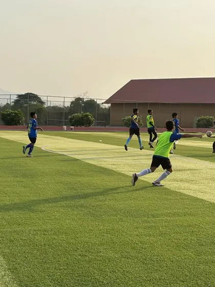 An evening training session in progress at the residential academy. The setting sun casts a golden light over the pitch as players engage in drills, showing that football is the start and end of every day here.