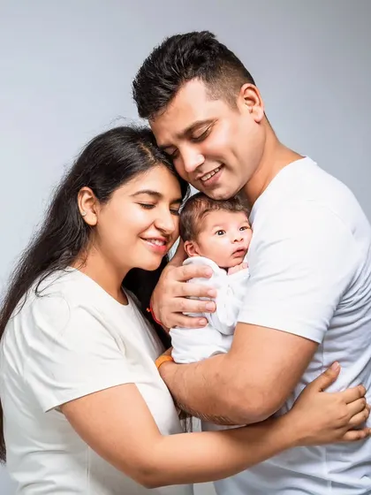 A classic and casual family portrait with both parents in white, lovingly holding their baby. This timeless style creates bright, clean images focused on your family.