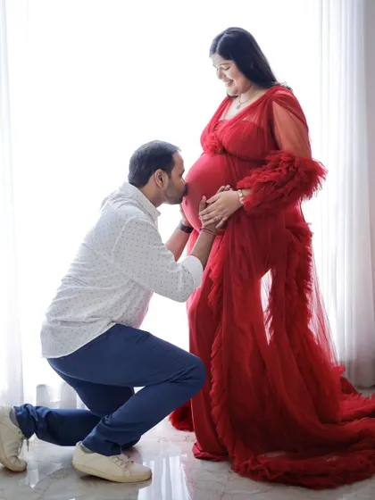 A classic pose of a partner kissing the baby bump, captured in a beautiful red gown. This is a timeless shot that many of our clients request.