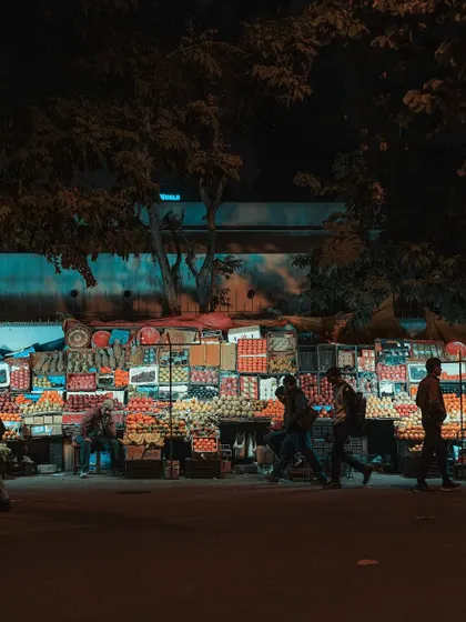A fruit stall illuminated at night. The vibrant colors of the fruit stand out against the darkness, creating a beacon of life and commerce.