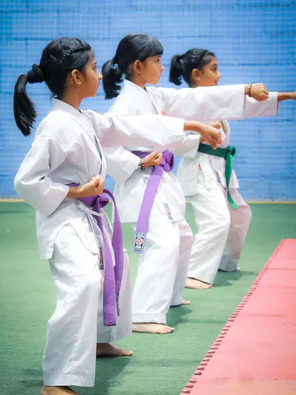 Three young girls demonstrate a synchronized punching technique, showing the precision and unity we foster in our group training sessions for belt examinations.