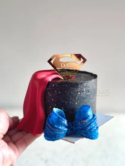 A handheld view of the Superman-themed bento cake. You can see the details of the fondant cape and bow tie, making it a fun and memorable cake for any dad.
