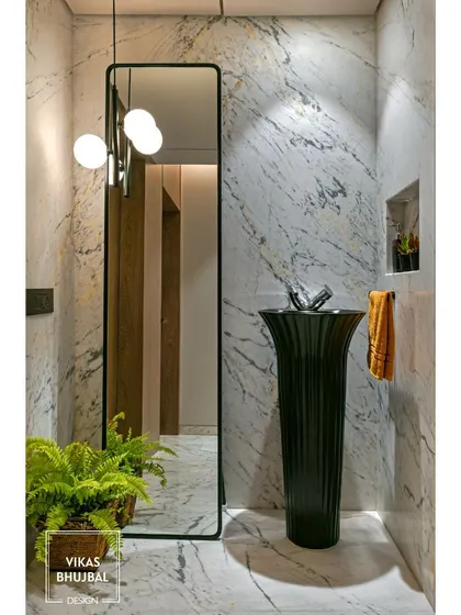 This powder room makes a bold statement with a freestanding black pedestal sink against a white marble wall. A full-length mirror and a modern pendant light add to the dramatic and stylish look.