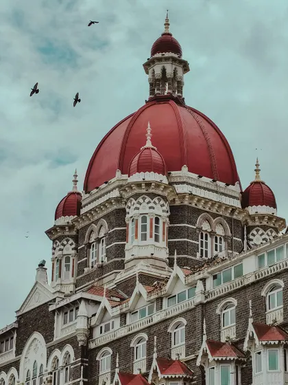 The iconic red dome of the Taj Mahal Palace hotel, with birds flying past. A timeless symbol of Mumbai's grandeur.