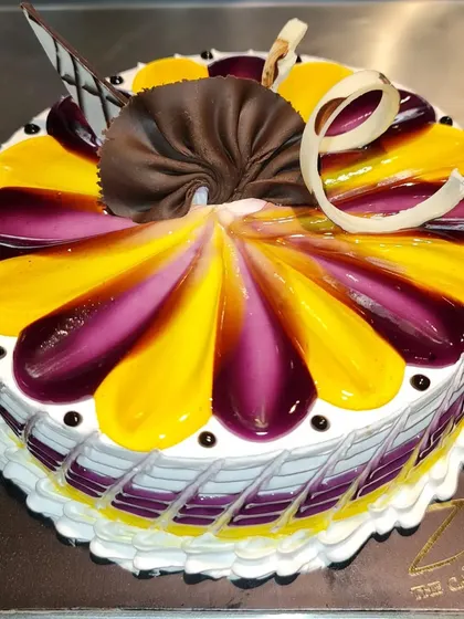 A vibrant mango blueberry cake. The top is decorated with a beautiful petal pattern of yellow mango and purple blueberry glazes.