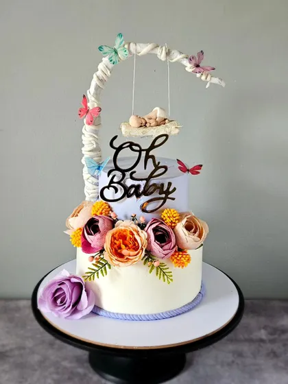 A dreamy baby shower cake with a floral swing. This design uses a delicate color palette and a mix of fresh and sugar flowers to create a beautiful, ethereal feel.