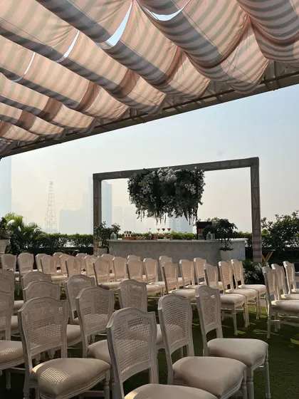 An elegant outdoor Haldi setup with white guest seating and a chic bar area under a canopy of green and white florals.