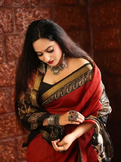 A model looking down, showcasing her elegant red and black saree and oxidized jewelry. This pose creates a sense of introspection and highlights the beautiful drape of the fabric.