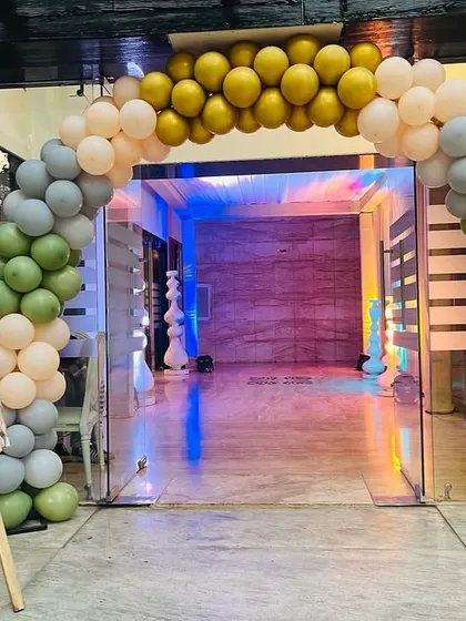 An elegant balloon arch in muted green, grey, and peach tones for a subtle jungle-themed birthday party entrance. A custom welcome easel sign greets the guests at the door.