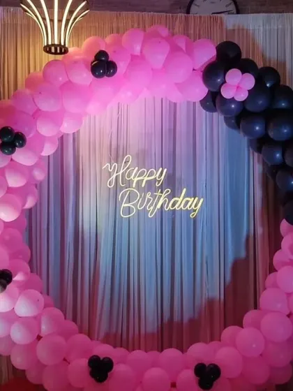 A modern pink and black circular balloon backdrop with a "Happy Birthday" sign, perfect for a stylish party.
