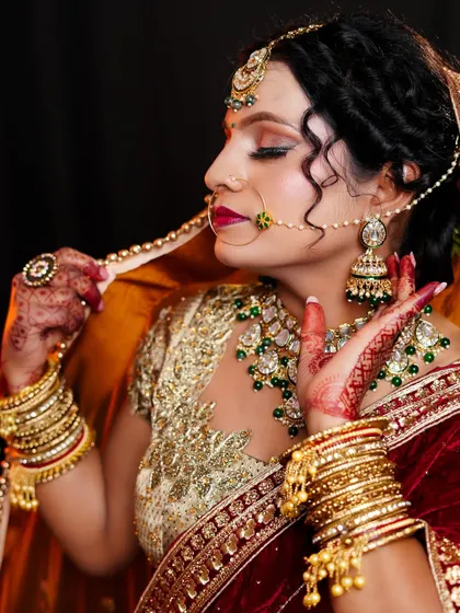 A close-up of a stunning bridal look focusing on the details. Notice the perfectly blended eyeshadow, the intricate nath design, and the way the jewellery complements the rich velvet and gold-embroidered outfit.