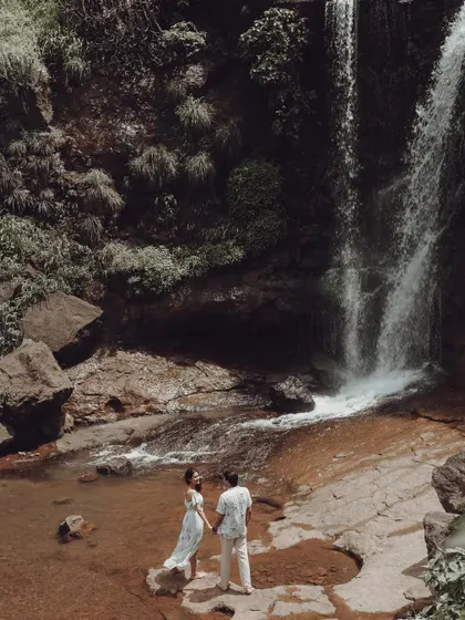 A beautiful pre-wedding shot with a couple standing by a waterfall, holding hands and surrounded by nature.