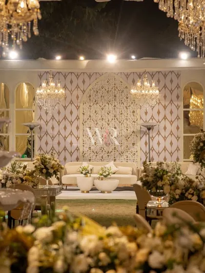A view of the lounge area for the all-white wedding. We created a stunning backdrop with a custom geometric jaali pattern, framed by elegant white drapes and lit by chandeliers, with a classic white fountain adding a touch of serenity.